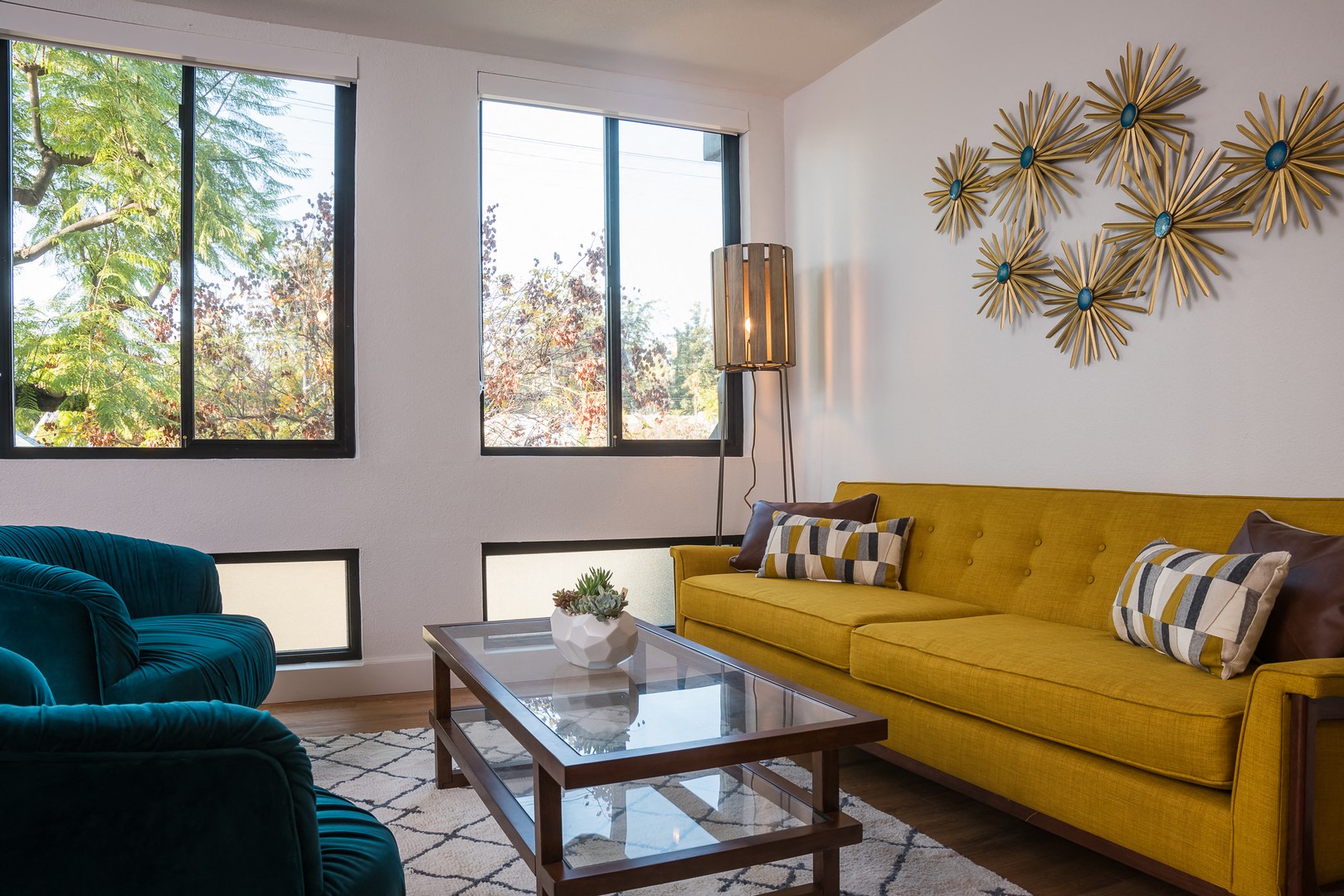 A living room with a yellow couch and a glass coffee table.