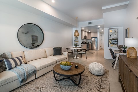 A living room with a white couch and a round mirror on the wall.