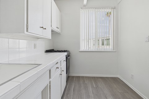 A kitchen with white cabinets and a window with blinds.