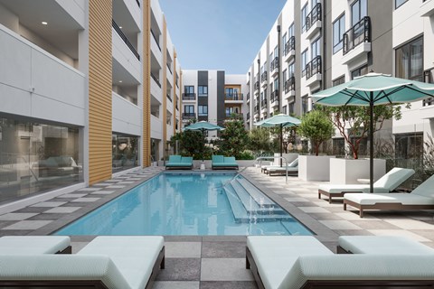 A swimming pool surrounded by lounge chairs and umbrellas in a courtyard.