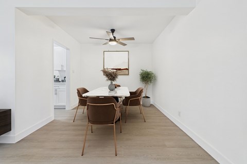 A dining room with a white table and brown chairs.