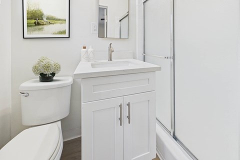 A white bathroom with a toilet, sink, and a framed picture on the wall.
