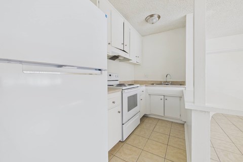 A white kitchen with a refrigerator, oven, and sink.