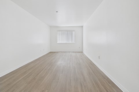A room with wooden flooring and a white wall with a vent.