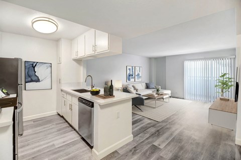 A modern kitchen with a refrigerator on the left and a dining area with a white couch and a coffee table.