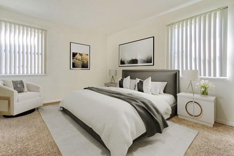 A bedroom with a large bed, a white armchair, and two framed pictures on the wall.