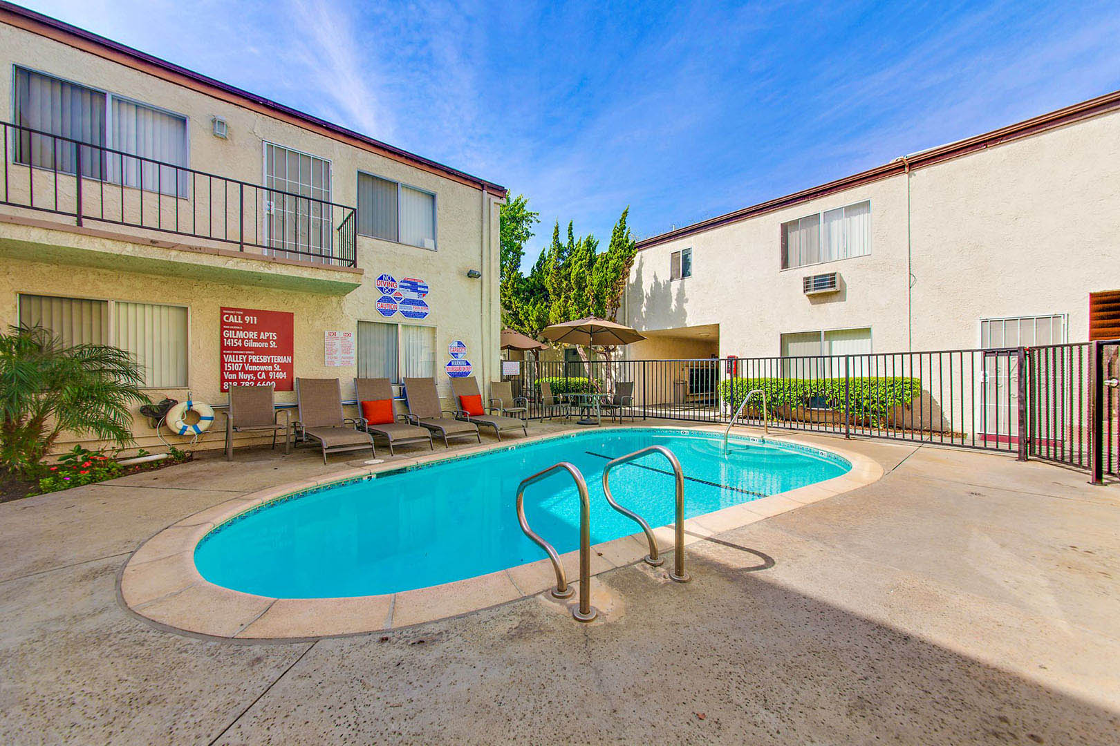 A pool surrounded by a fence and chairs in front of a building.