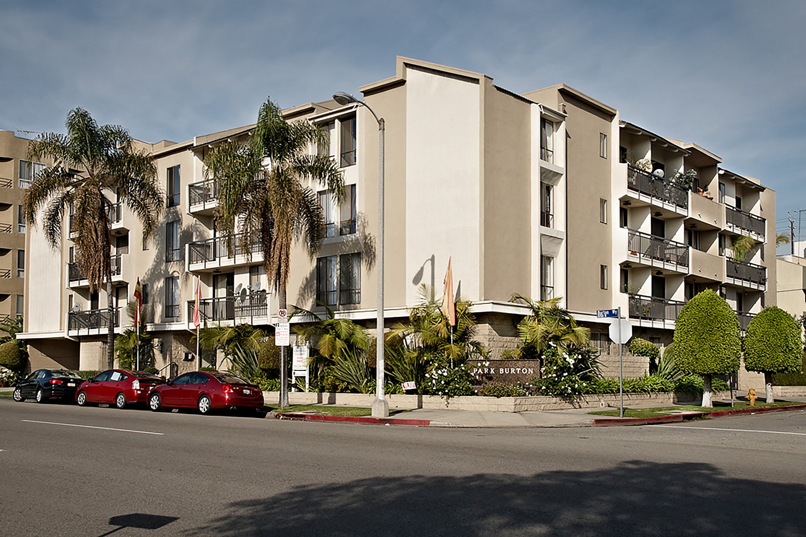 A row of apartment buildings with cars parked in front.