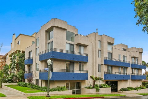 A large, modern building with blue balconies and a red curb.
