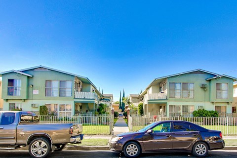 A brown sedan is parked on the street in front of a green apartment building.