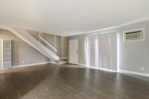 Living room with air conditioning on the right, wood-style flooring, vertical blinds, carpeted staircase to the second floor