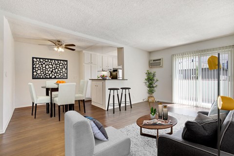 A living room with a grey couch, a coffee table, a dining table with chairs, and a kitchen area in the background.