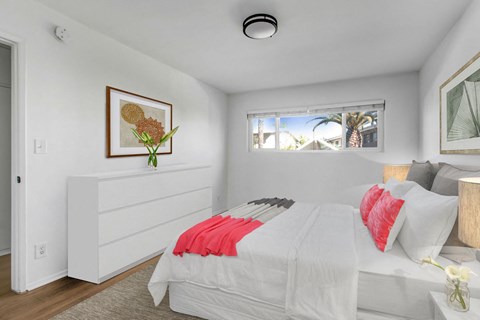A bedroom with a bed, nightstand, and a window with a view of a palm tree.