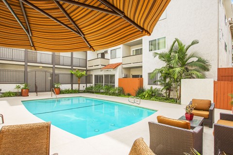 A pool surrounded by chairs and a brown umbrella.