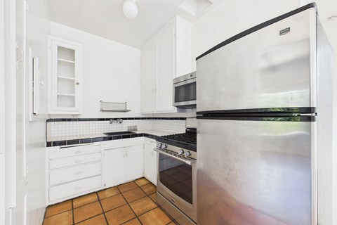 A kitchen with a stainless steel refrigerator and black countertops.