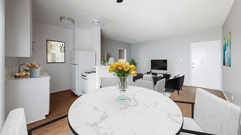 A white marble table with a vase of yellow flowers is in the middle of a white kitchen and dining room.