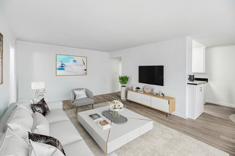 A living room with a white couch, a grey coffee table, a television, and a painting on the wall.