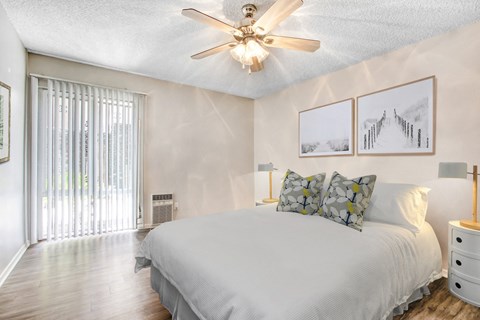 A bedroom with a bed, pillows, a ceiling fan, and pictures on the wall.