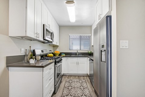 A kitchen with white cabinets and a black and white patterned rug on the floor.