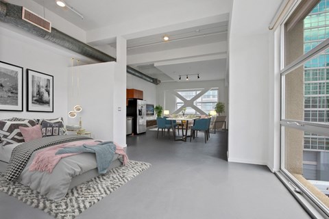 A modern bedroom with a large bed and a dining area in the background.
