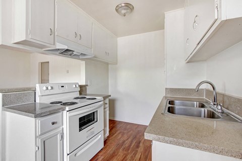 A kitchen with a stove, sink, and cabinets.