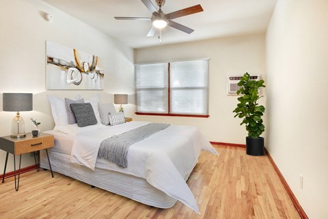 A bedroom with a bed, a ceiling fan, and a potted plant.