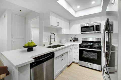 a white kitchen with stainless steel appliances and white counter tops