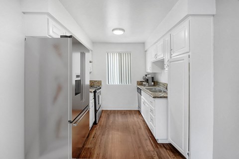 A white kitchen with a refrigerator on the left and a sink with a counter on the right.