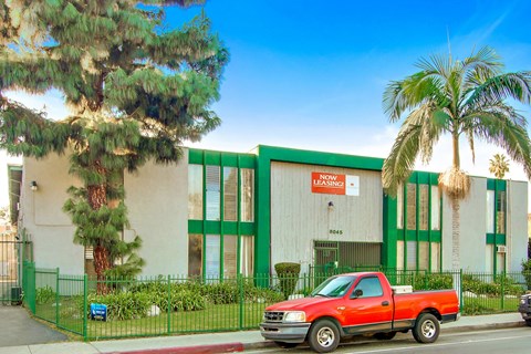 A red pickup truck is parked in front of a building with a green fence.