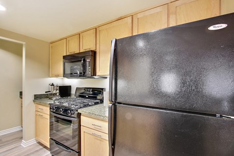 A black refrigerator in a kitchen with wooden cabinets.