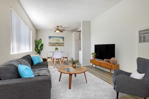 A living room with a grey couch, a wooden coffee table, a grey armchair, a flat screen TV, and a painting on the wall.