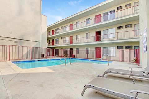 A pool area with sun loungers and apartment buildings in the background.