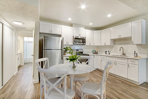 A kitchen with white cabinets and a dining table with chairs.