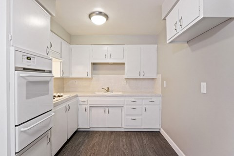 A white kitchen with wood flooring and a white refrigerator.