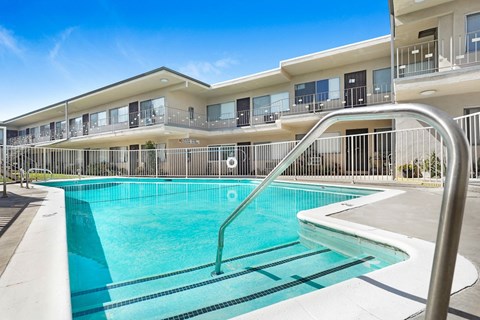 A swimming pool in front of a building with a metal railing.