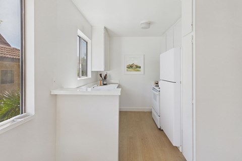 A small white kitchen with a fridge, sink and window.