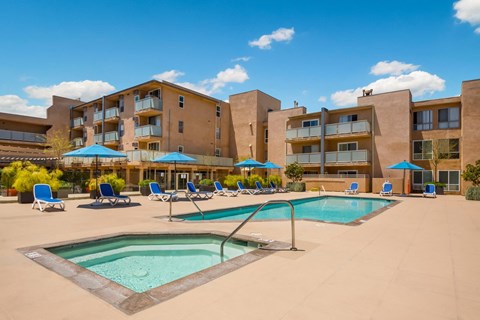 A swimming pool surrounded by sun loungers and umbrellas in front of a building.