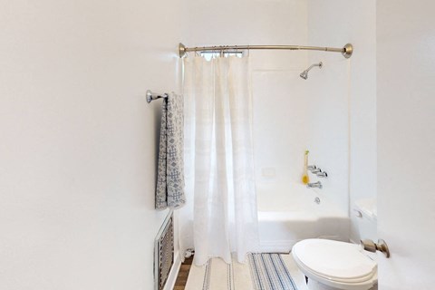 A white toilet sits in a bathroom with a white shower curtain.
