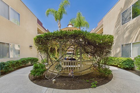 A tree-covered gazebo is in the middle of a courtyard.