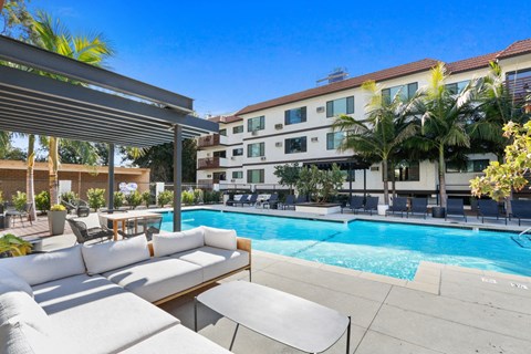 a pool with lounge chairs and tables and a building in the background