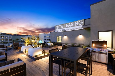 A rooftop patio with a table and chairs and a grill.
