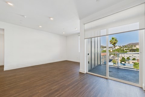 A room with a sliding glass door leading to a balcony with a view of a building and a palm tree.