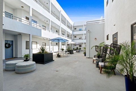 A sunny day at the courtyard of a white building with blue umbrellas and potted plants.