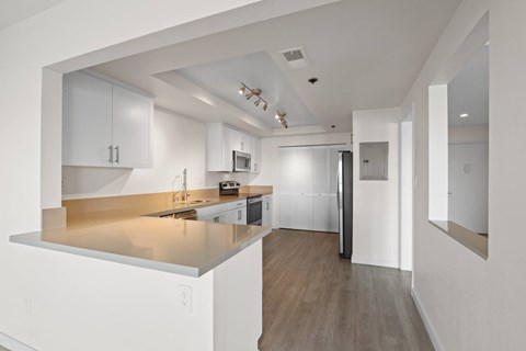 A modern kitchen with white cabinets and a wooden floor.