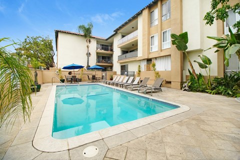 A swimming pool in a courtyard surrounded by chairs and umbrellas.