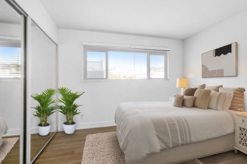 A bedroom with a large bed and two potted plants.
