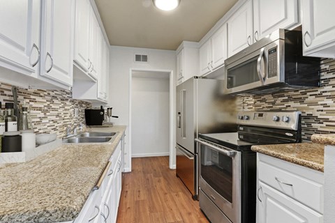A kitchen with white cabinets and a stone backsplash.