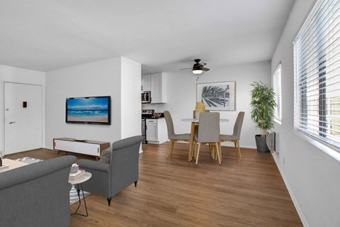 A living room with a grey couch, a dining table with chairs, a ceiling fan, and a painting on the wall.