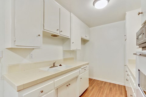 Kitchen with White kitchen cabinets and cupboards, Double white kitchen sink and Tile countertops on the right side, White Oven on the left side