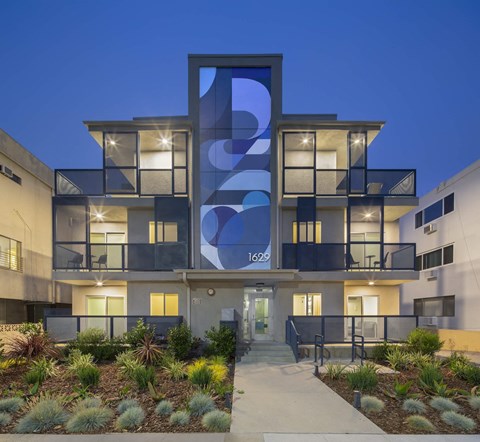 Modern apartment facade with illuminated units at twilight at Cypress Co-Living Apartments, Los Angeles, 90024